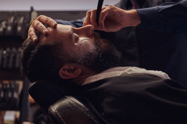 Kuaför sakalını tehlikeli bir ustura ile tıraş ederken erkek Kuaför Salonu bir koltukta otururken yakışıklı bir hipster sakallı.