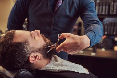 Erkek Kuaför Salonu Kuaför modelleme sakal iken bir koltukta makas ve tarak ile berber dükkanında oturmuş sakallı.