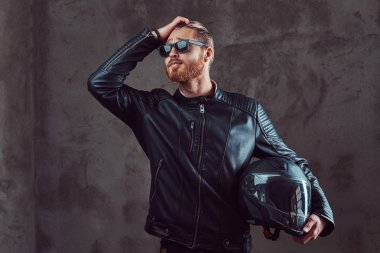 Bir siyah deri ceket ve güneş gözlüğü, yakışıklı şık Kızıl motorcu portresi tutan bir stüdyoda poz motosiklet kask.