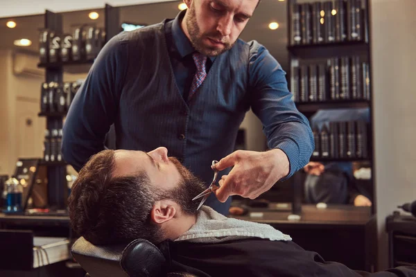 Professionell frisör modellering skägg med sax och kam på barbershop. — Stockfoto