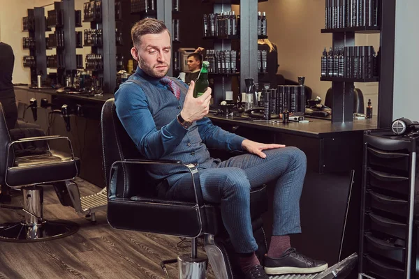 Професійний перукар, сидячи на кріслі, відпочиває після роботи з пляшкою пива в руці . — стокове фото