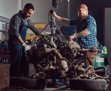 İki sakallı mekaniği uzman Hidrolik Asansör garaja kaldırdı arabanın motoru onarır. Servis istasyonu.