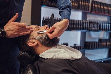 Kuaför sakalını tehlikeli bir ustura ile tıraş ederken erkek Kuaför Salonu bir koltukta otururken yakışıklı bir hipster sakallı.