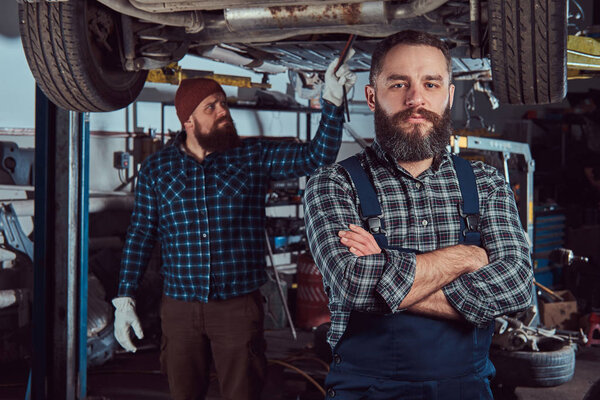 Two bearded brutal mechanics repair a car on a lift in the garage. Repairing car suspension.