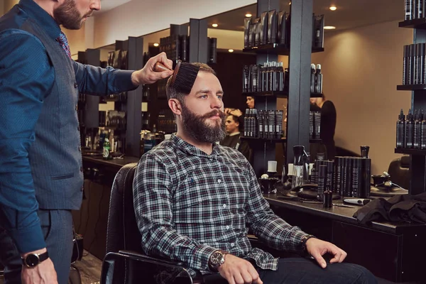 Hipster man in a barber shop. Professional hairdresser uses a brush, almost finished hairstyle.