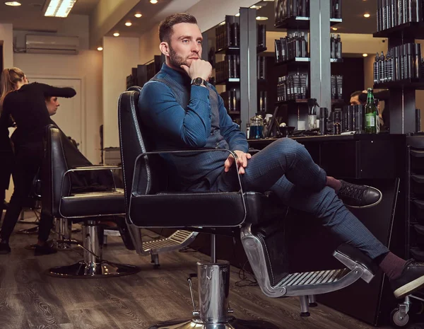 A professional hairdresser sitting on a barber chair, waiting for the next customer.