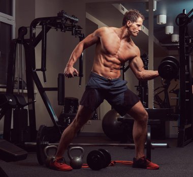 Spor salonunda dumbbells ile bir pazı egzersizleri yaparken kas vücut geliştirmeci adam.
