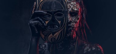 Taşlaşmış bir kırık Cilt ve dreadlocks, korkutucu Afrika şaman erkek portresi geleneksel maske karanlık bir arka plan üzerinde tutar. Kalıcı makyaj kavramı.