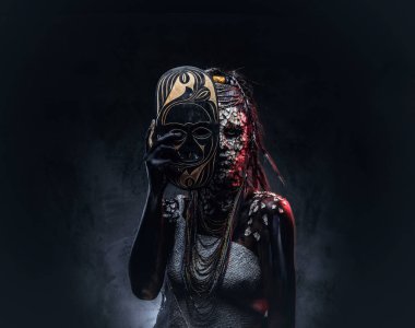 Taşlaşmış bir kırık Cilt ve dreadlocks, korkutucu Afrika şaman erkek portresi geleneksel maske karanlık bir arka plan üzerinde tutar. Kalıcı makyaj kavramı.