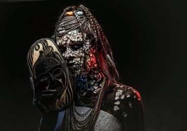 Taşlaşmış bir kırık Cilt ve dreadlocks, korkutucu Afrika şaman erkek portresi geleneksel maske karanlık bir arka plan üzerinde tutar. Kalıcı makyaj kavramı.