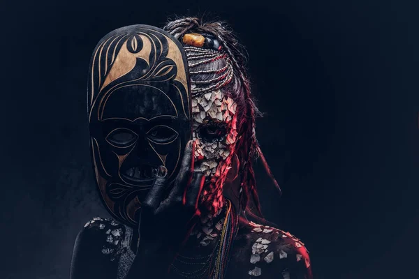 石化したひびの入った肌とドレッドヘア アフリカのシャーマンが怖い女性の肖像画は 暗い背景に伝統的なマスクを保持します メイクのコンセプト — ストック写真