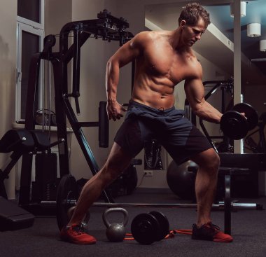 Spor salonunda dumbbells ile bir pazı egzersizleri yaparken kas vücut geliştirmeci adam.