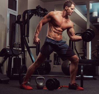 Spor salonunda dumbbells ile bir pazı egzersizleri yaparken kas vücut geliştirmeci adam.