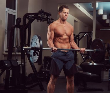 Kas gömleksiz vücut geliştirmeci erkek üzerinde bir pazı bir spor salonunda bir halter kaldırma.