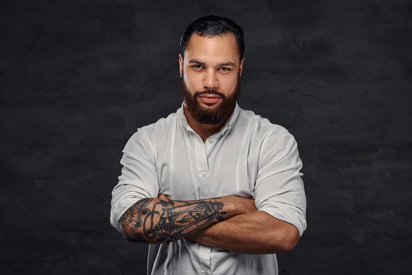 Portrait of a handsome African-American tattooed man with stylish hair and beard, stands with crossed arms.