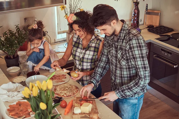 Linda niña y sus hermosos padres preparan pizza mientras cocinan en la cocina en casa . —  Fotos de Stock