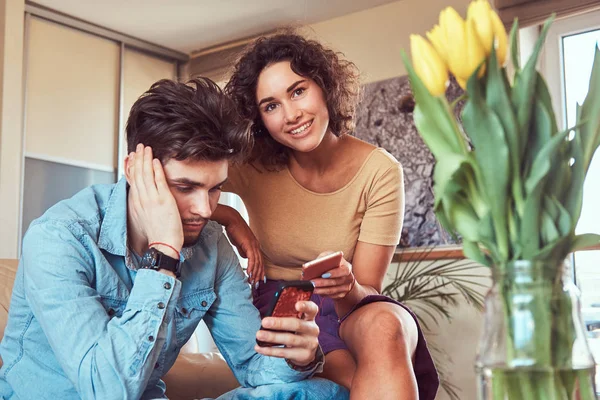 Casal hispânico relaxando juntos no sofá. Usando smartphones enquanto descansa em casa . — Fotografia de Stock