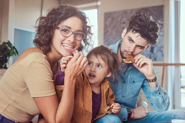 Pequeno-almoço familiar. Jovem família atraente tomando café da manhã em casa sentado em um sofá . — Fotografia de Stock