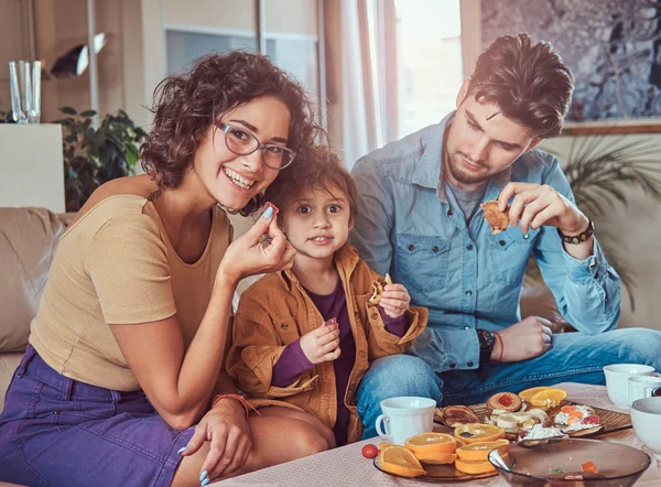 Desayuno familiar. Joven familia atractiva desayunando en casa sentado en un sofá . —  Fotos de Stock