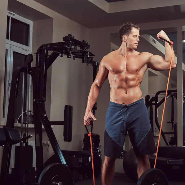 Muskulöser, hemdsloser Athlet, der im Fitnessstudio mit einem Expander trainiert. — Stockfoto