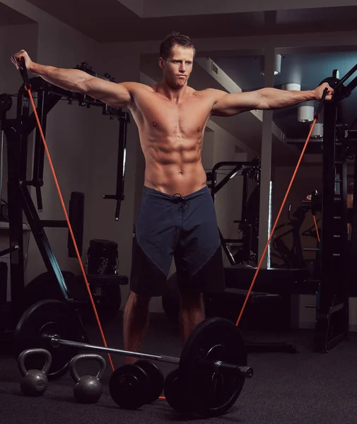 Atleta sem camisa muscular fazendo exercício com um expansor no ginásio . — Fotografia de Stock