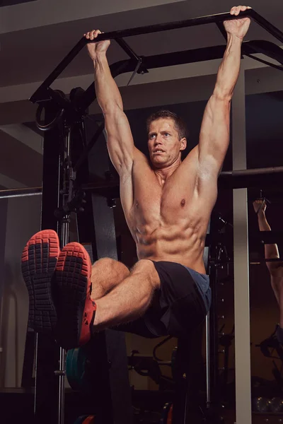 Musculoso hombre sin camisa haciendo flexiones en la barra horizontal en el gimnasio . —  Fotos de Stock