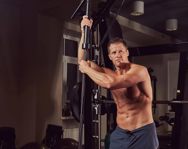 Musculoso hombre sin camisa posando con una barra en el gimnasio . —  Fotos de Stock