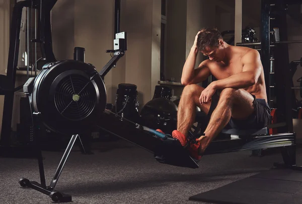 Kas gömleksiz atlet spor salonunda kürek makine üzerinde oturur iken sert bir çalışmadan sonra dinlenme. — Stok fotoğraf