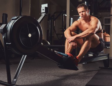 Kas gömleksiz atlet spor salonunda kürek makine üzerinde oturur iken sert bir çalışmadan sonra dinlenme.