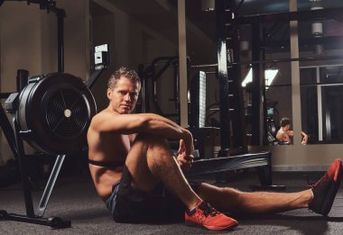 Kas gömleksiz atlet spor salonunda sert bir çalışmadan sonra dinlenme bir katta oturur.