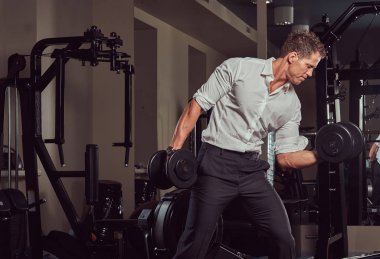 Resmi kıyafetler spor salonunda dumbbells ile egzersiz yaparak yakışıklı kaslı işadamı.