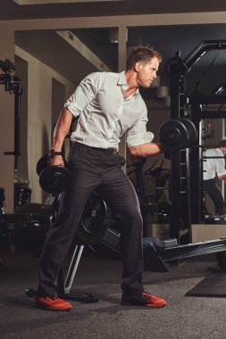 Resmi kıyafetler spor salonunda dumbbells ile egzersiz yaparak yakışıklı kaslı işadamı.