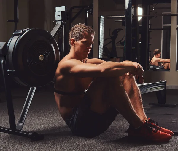 Kas gömleksiz atlet spor salonunda sert bir çalışmadan sonra dinlenme bir katta oturur.