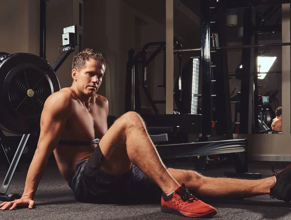 Kas gömleksiz atlet spor salonunda sert bir çalışmadan sonra dinlenme bir katta oturur.