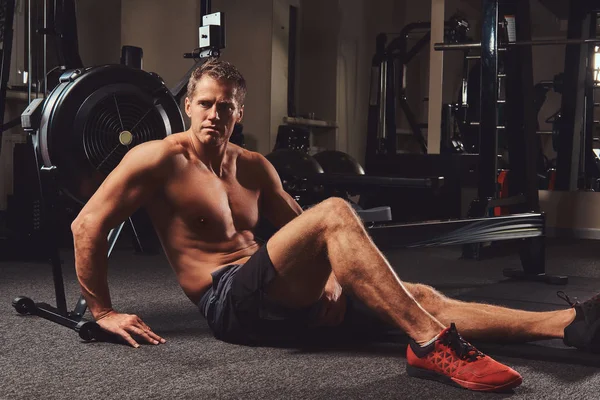 Kas gömleksiz atlet spor salonunda sert bir çalışmadan sonra dinlenme bir katta oturur.