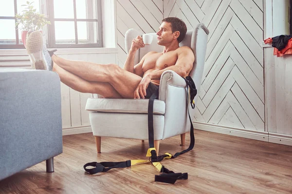 英俊的无上衣肌肉男子躺在椅子上 喝杯茶 休息后 在家里的艰苦锻炼 — 图库照片