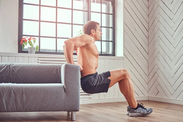 Handsome Shirtless Muscular Man Does Exercise Leaning Sofa Home — Stock Photo, Image