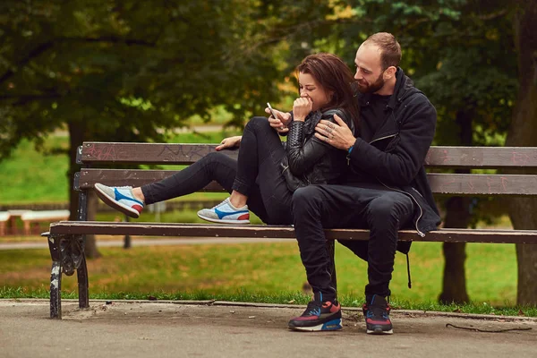 快乐的现代情侣 在公园的长凳上拥抱 在网上浏览一些有趣的东西 享受他们的爱和自然 — 图库照片