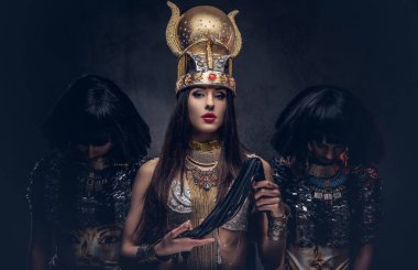 Bir eski firavun kostüm iki cariye ile kibirli Mısır Kraliçesi portresi. Karanlık bir arka plan üzerinde izole.
