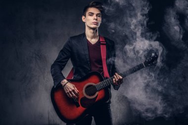 Şık giysileriyle şık saç ile oynama ve karanlık bir arka plan üzerinde poz onun elinde bir gitar ile şık genç müzisyen.