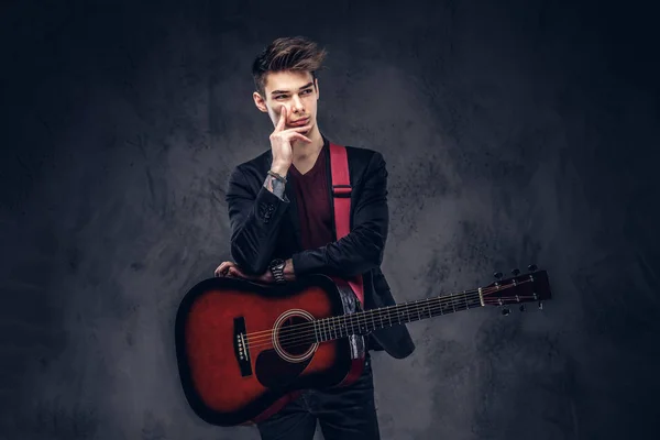 英俊的年轻体贴的音乐家与时髦的头发穿着优雅的衣服摆在他手中的吉他 在黑暗背景下被隔离 — 图库照片
