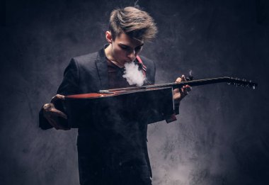 Şık giysileriyle exhales onun akustik gitar üzerinde duman içinde şık saçlı yakışıklı genç müzisyen.