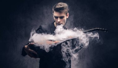 Şık giysileriyle exhales onun akustik gitar üzerinde duman içinde şık saçlı yakışıklı genç müzisyen.