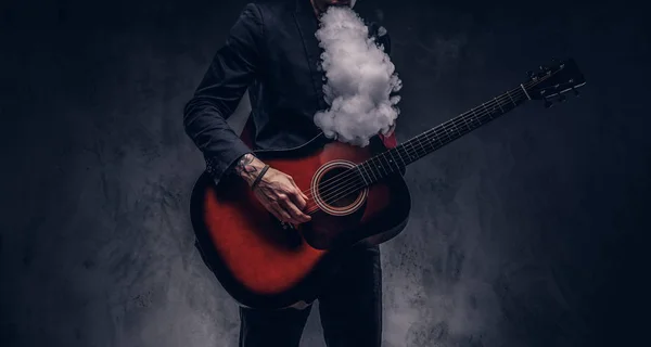 Stijlvolle muzikant in elegante kleding uitademt rook tijdens het spelen van akoestische gitaar. — Stockfoto