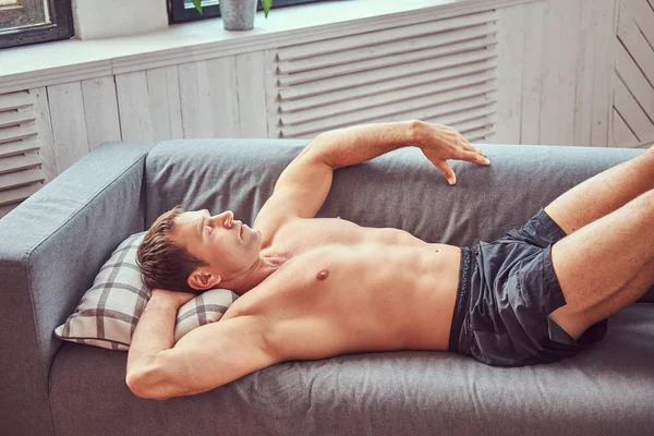 Yakışıklı gömleksiz kaslı adam sert bir çalışmadan sonra evde istirahat kanepede yatan. — Stok fotoğraf