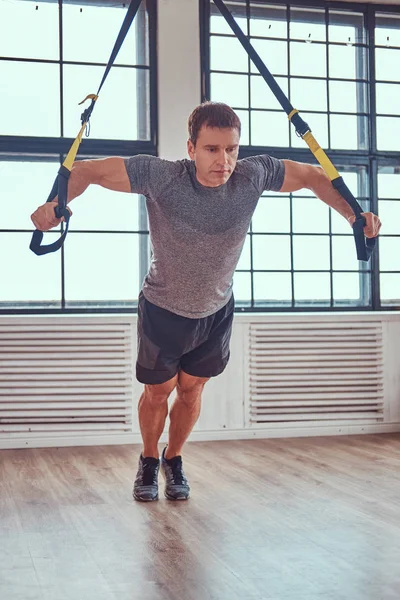 Homme de fitness musculaire faisant de l'exercice avec TRX. Entraînement fonctionnel à la maison avec des boucles TRX . — Photo
