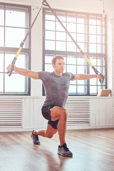 Muscular fitness male doing exercise with TRX. Functional workout at home with TRX loops.