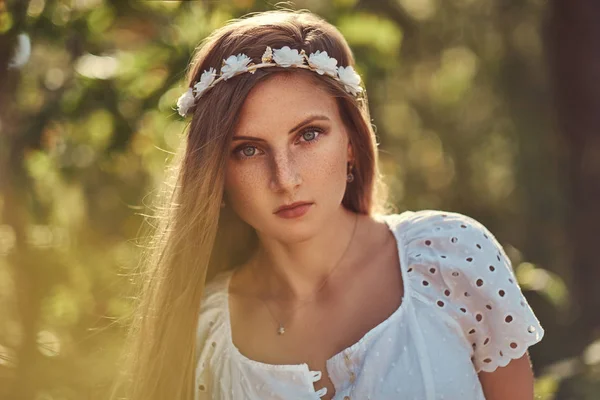 Una hermosa mujer en un vestido blanco y corona blanca en la cabeza posando en un bosque verde de otoño . — Foto de Stock