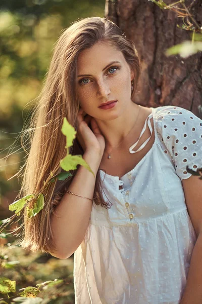 Charmante schöne Frau in einem weißen Kleid posiert in einem grünen Herbstwald. — Stockfoto