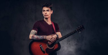 Yakışıklı genç müzisyen bir t-shirt onun elinde bir gitar ile poz içinde şık saç ile.